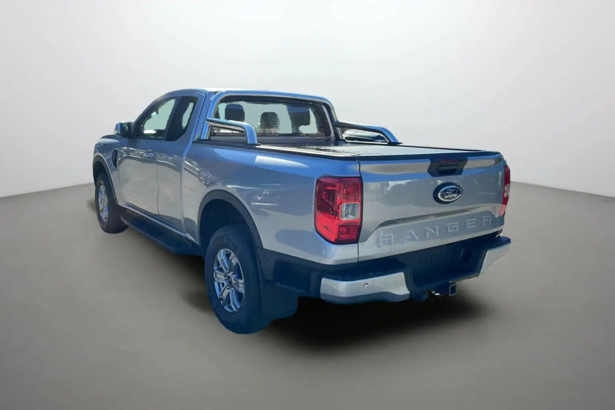 Ford Ranger gris iconic en 3/4 arrière droit avec arceaux inox et rideau coulissant de benne visible.