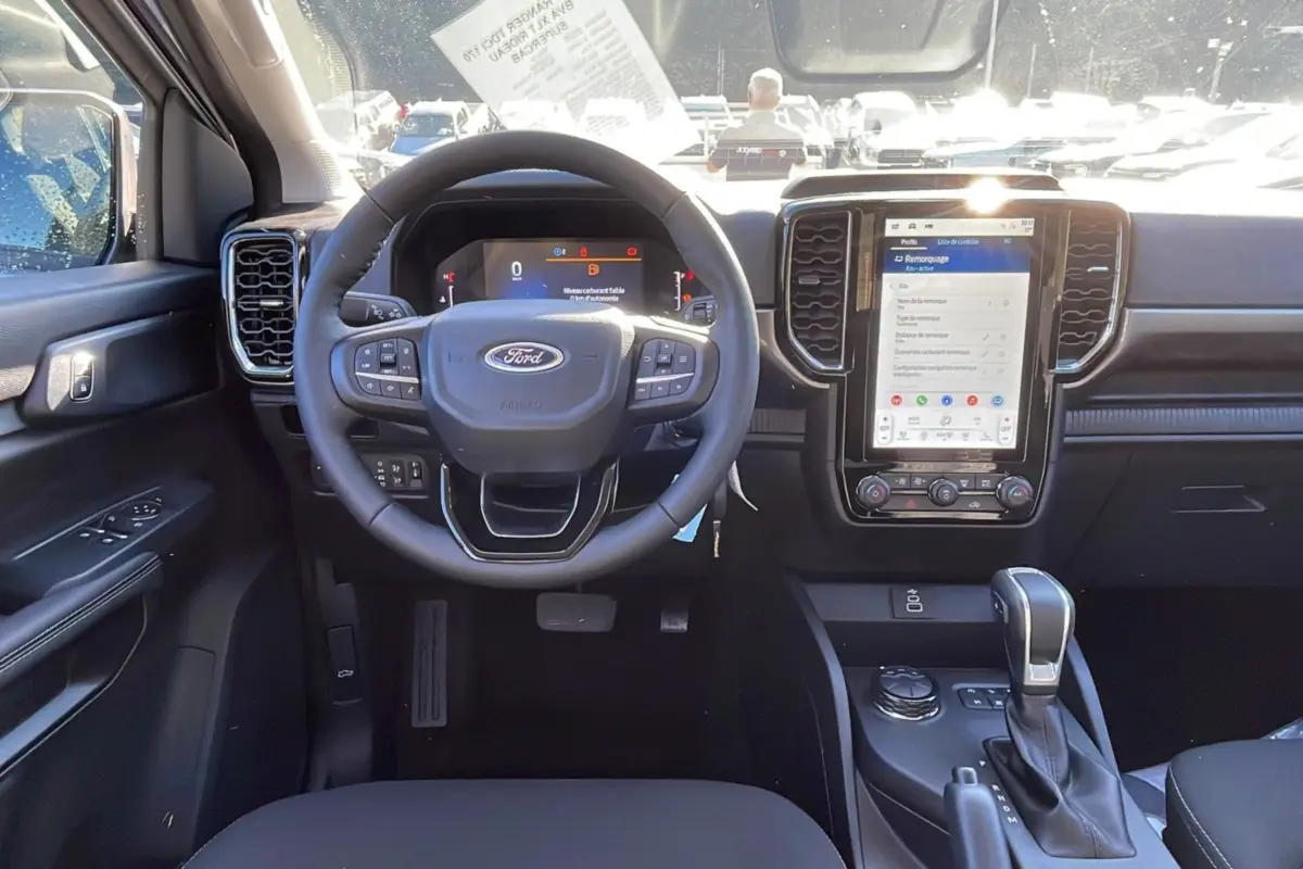 Vue intérieure avant du Ford Ranger 2025 avec tableau de bord noir, volant multifonctions et écran tactile vertical.