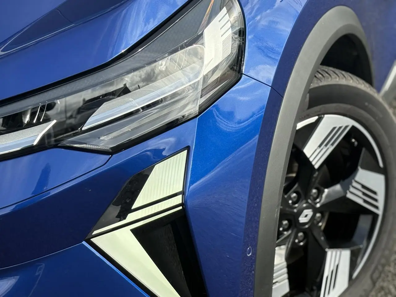Gros plan sur l'avant droit bleu Iron du Renault SYMBIOZ 2025, mettant en valeur le phare LED et la jante 18 pouces.
