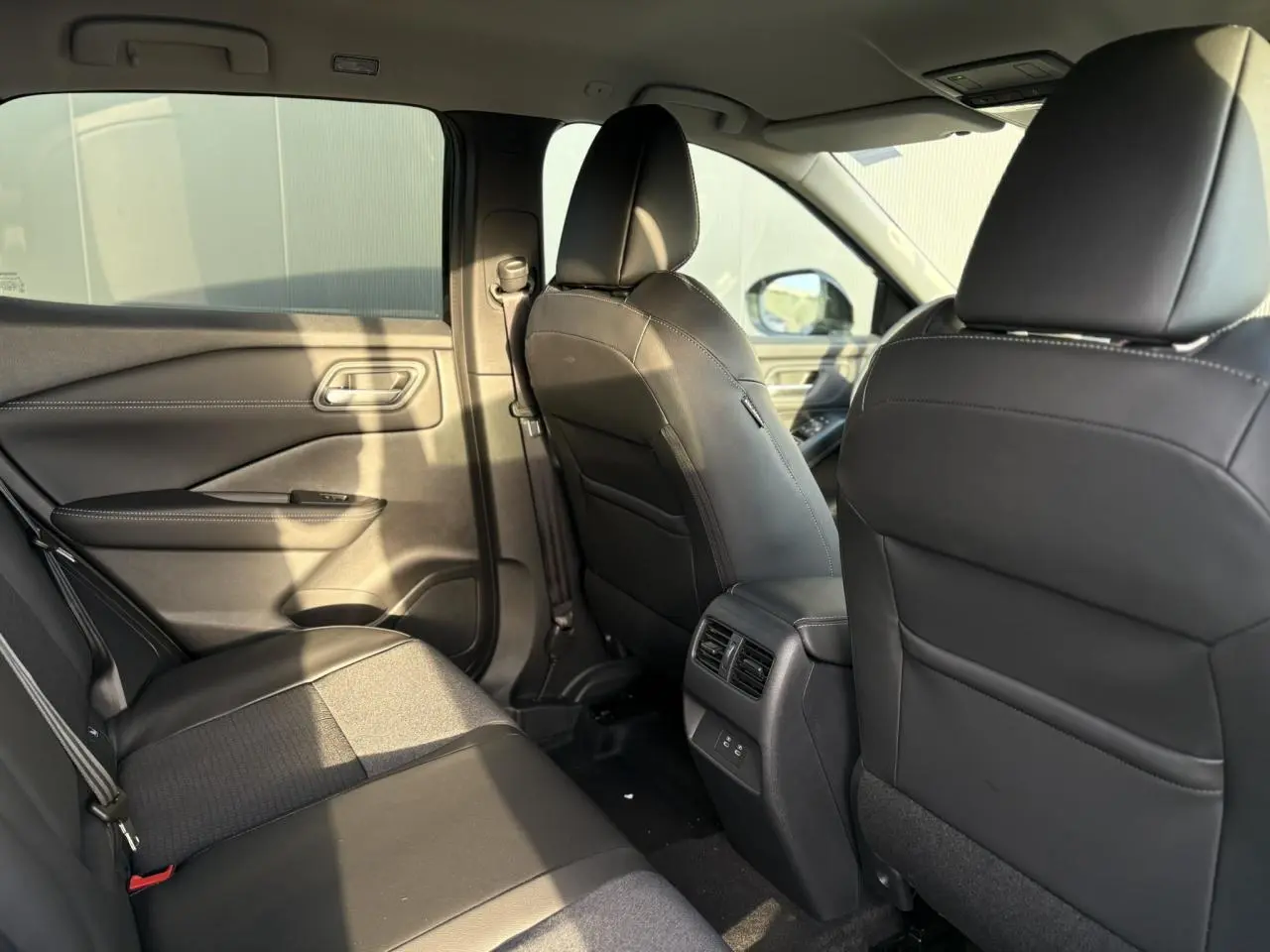 Vue intérieure arrière du Nissan Qashqai 2026 noir Kuro, sièges en cuir et tissu avec aérateurs centraux et ports USB.