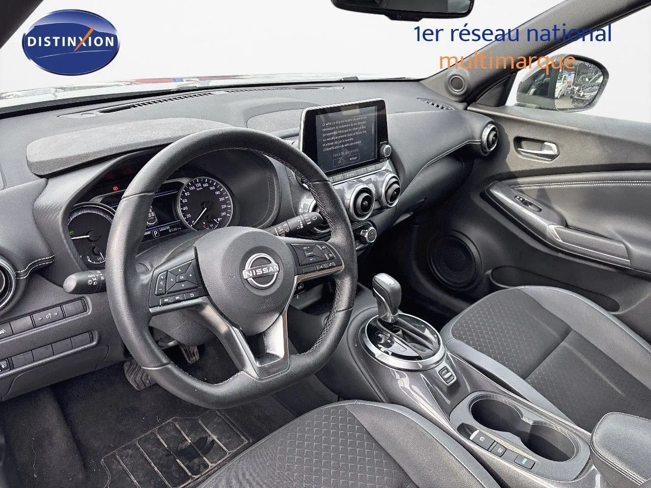 Intérieur avant droit du Nissan Juke 2024 gris perle, volant multifonction, écran tactile et console centrale avec boîte auto.
