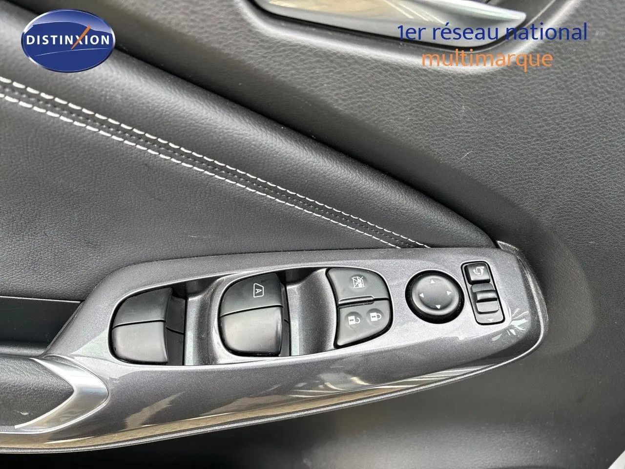 Gros plan sur la commande des vitres côté gauche en plastique gris perle métal avec surpiqûres blanches sur la portière du Nissan Juke 2024.