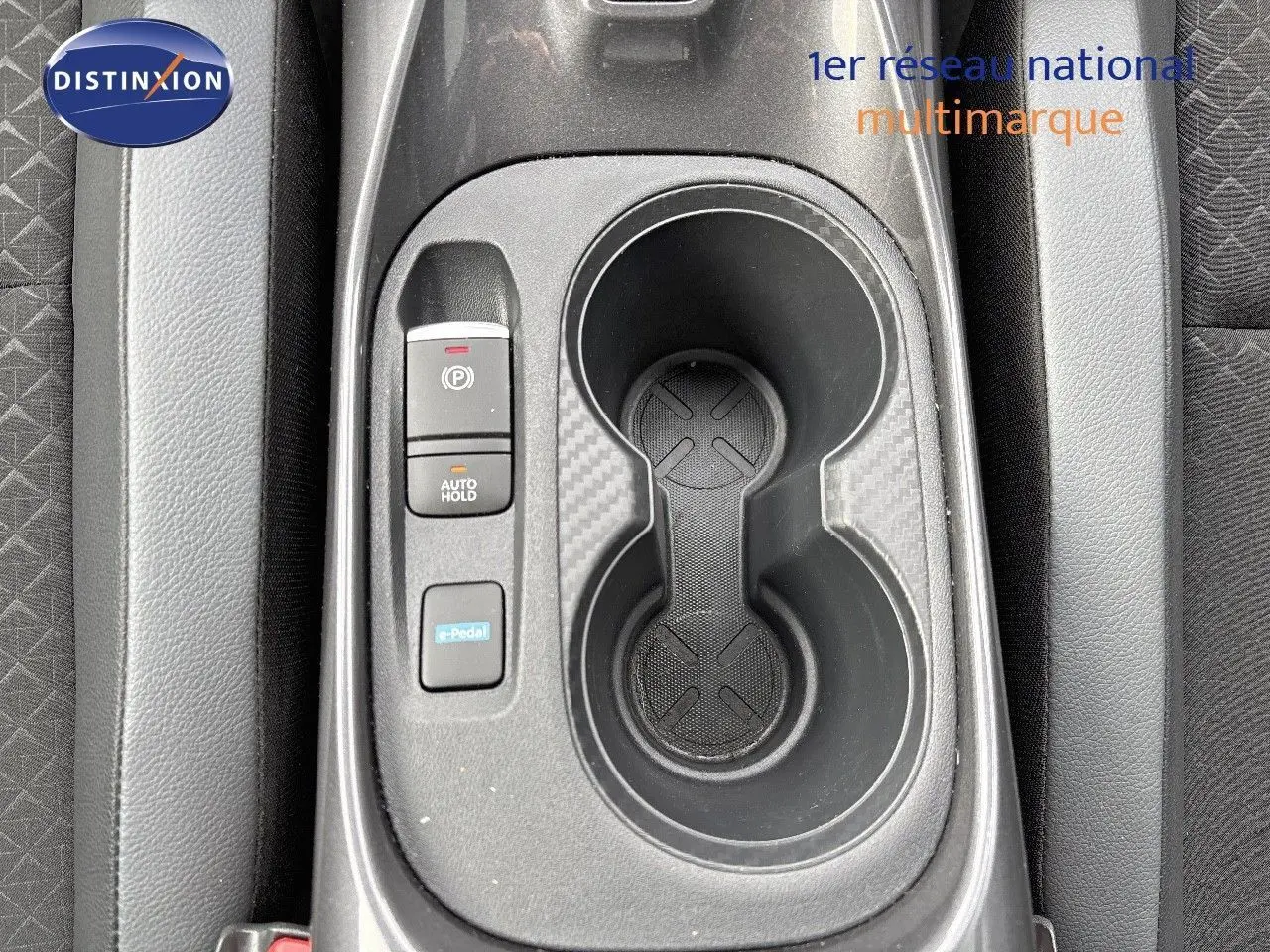 Gros plan sur la console centrale du Nissan Juke 2024 gris perle, montrant porte-gobelets et commandes électroniques.