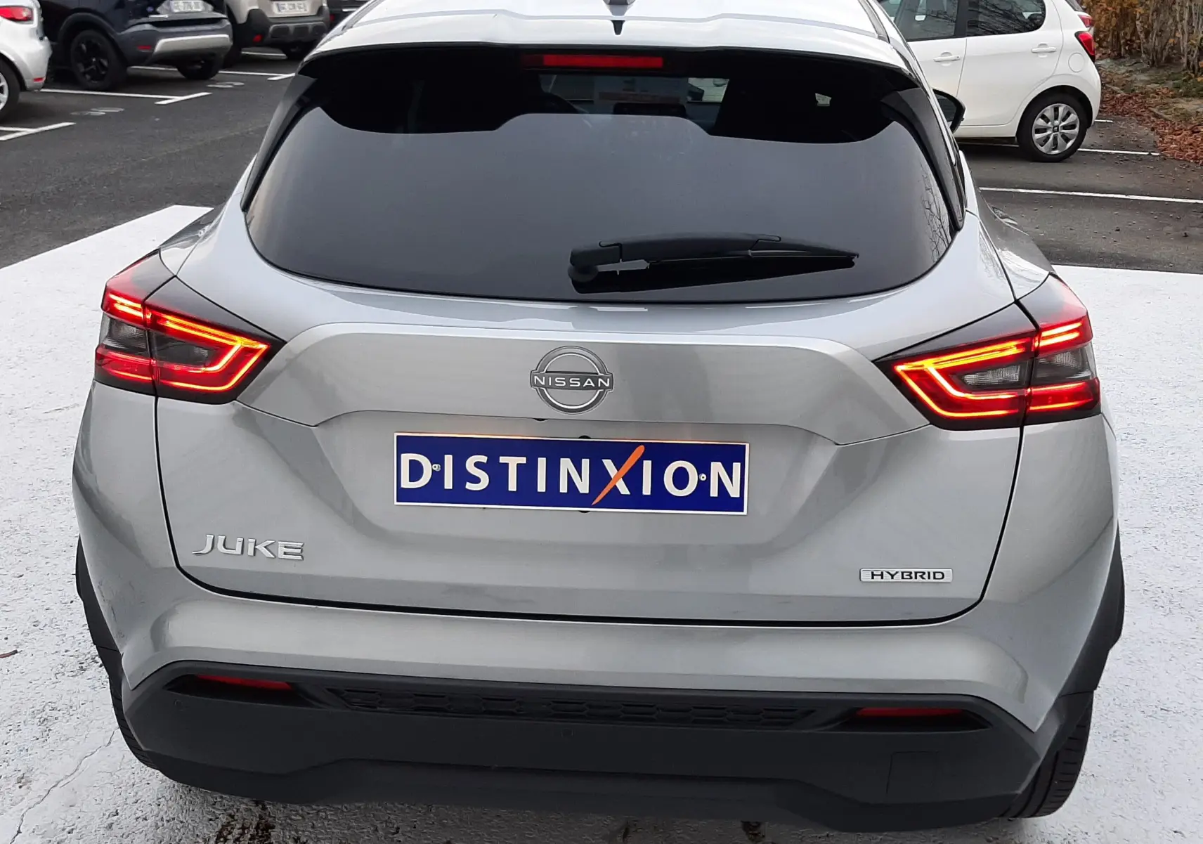Vue arrière d'un Nissan Juke gris perle métal 2024 avec feux LED allumés et badge Hybrid visible.