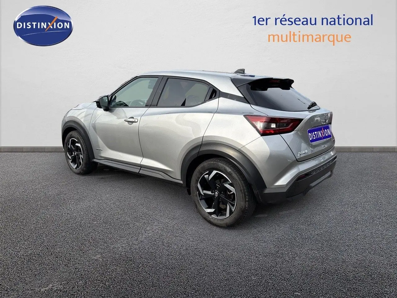 Nissan Juke gris perle métal vu en 3/4 arrière côté gauche, avec jantes noires et toit noir contrasté.