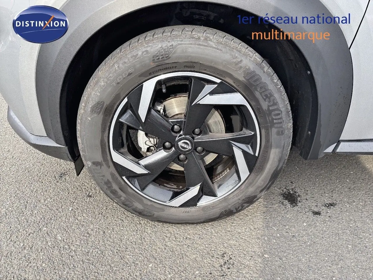 Gros plan sur la roue avant droite du Nissan Juke 2024 gris perle métal avec jante noire et grise au design géométrique.