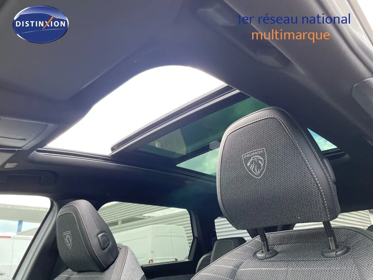 Vue intérieure du Peugeot 5008 Hybrid 2025 montrant les sièges avant en cuir noir avec logo et toit panoramique ouvert.