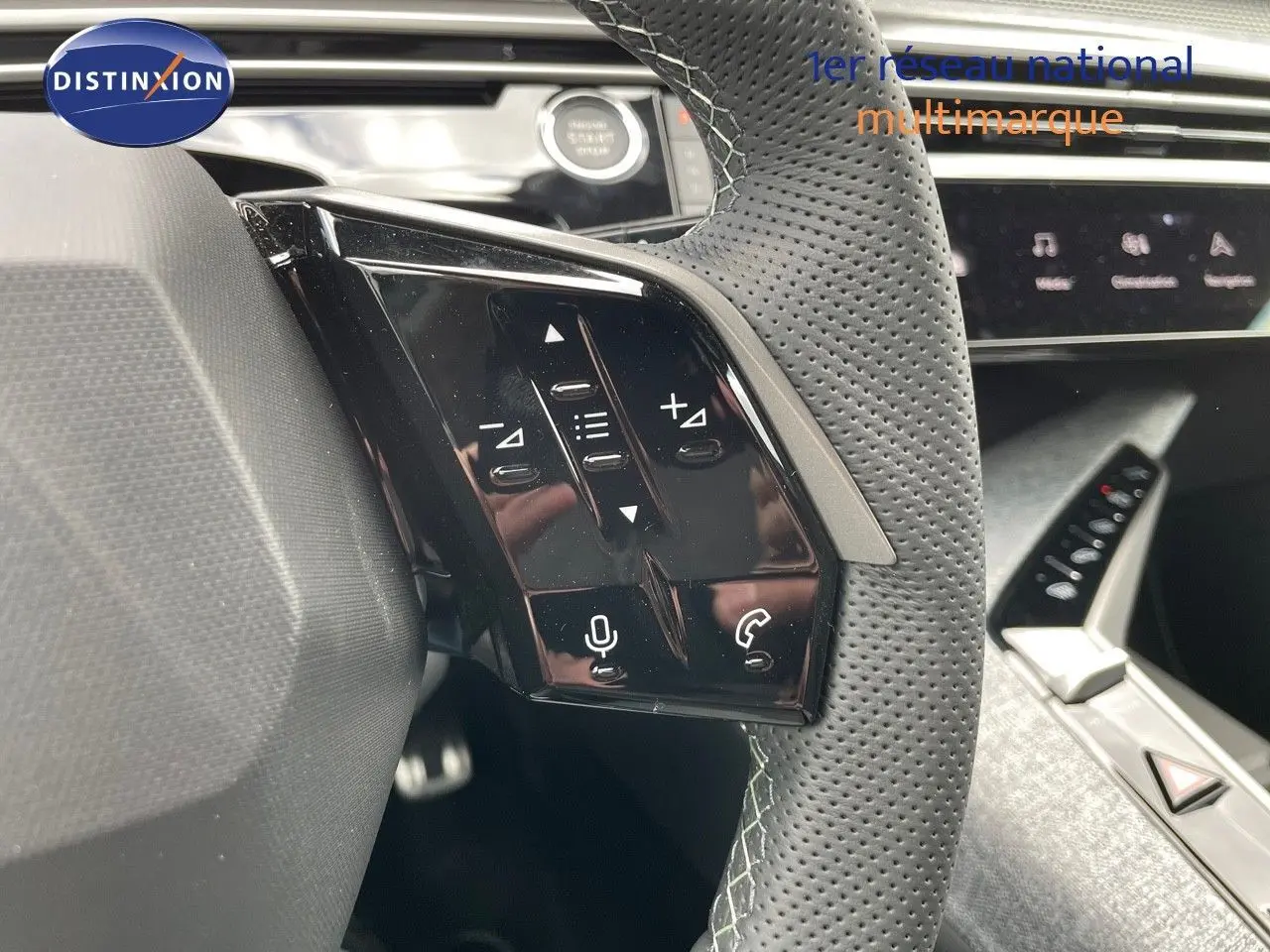 Gros plan sur les commandes au volant en cuir perforé du Peugeot 5008 Hybrid blanc Okenite métal avec toit noir, intérieur moderne.