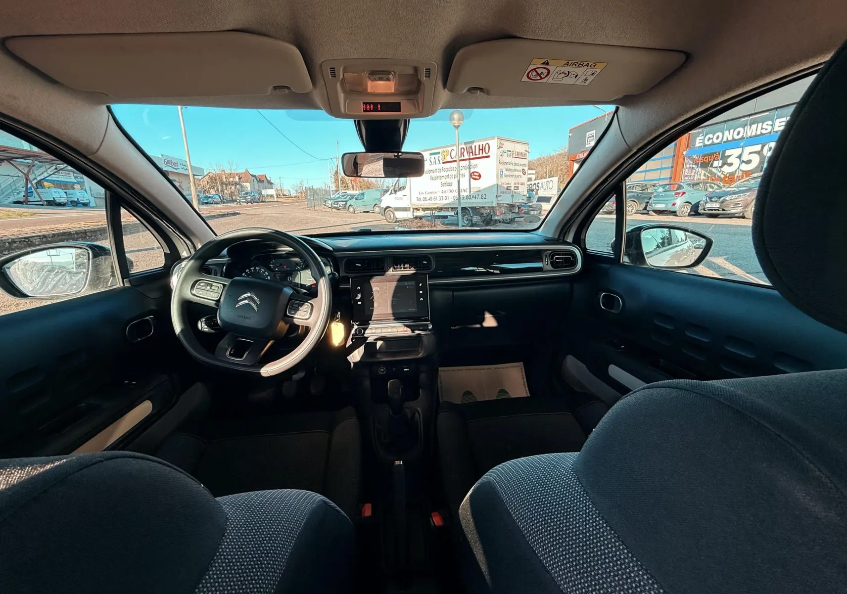 Vue intérieure avant de la Citroën C3 2017, tableau de bord et volant noir avec sièges tissu gris foncé.