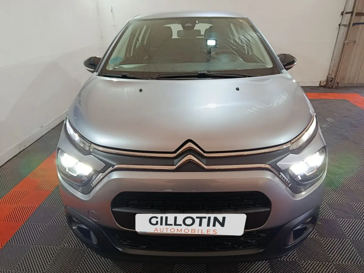 Vue avant d'une Citroën C3 2024 gris clair avec phares LED allumés dans un garage.