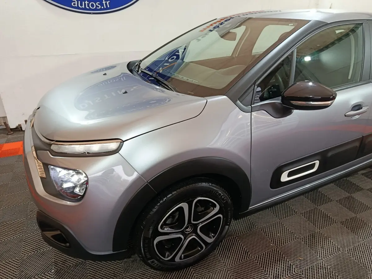 Vue 3/4 avant droit d'une Citroën C3 gris clair avec protections latérales noires et jantes alliage distinctives.