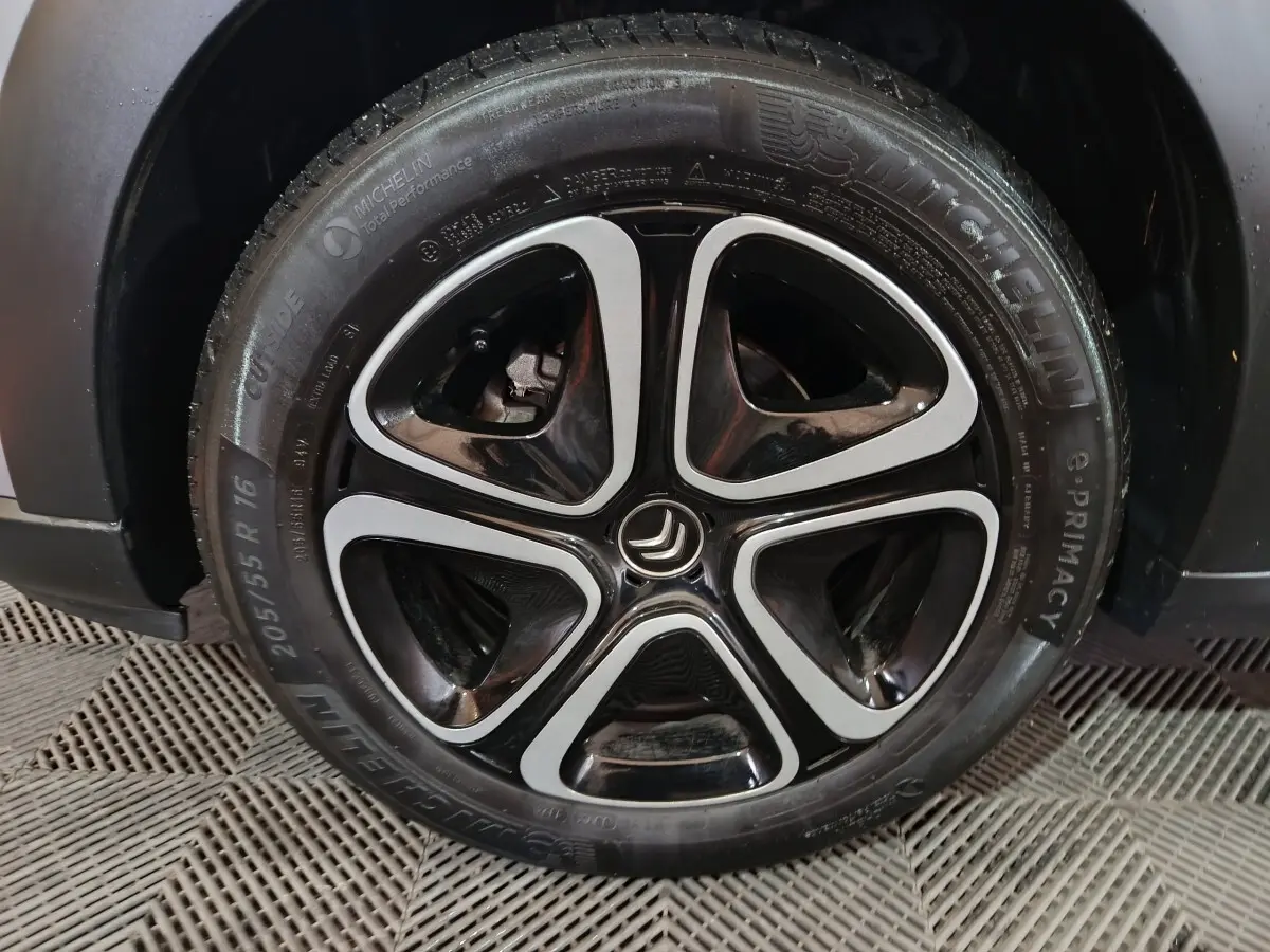 Gros plan sur la roue avant droite d'une Citroën C3 gris clair avec jante alliage noire et argentée au design moderne.