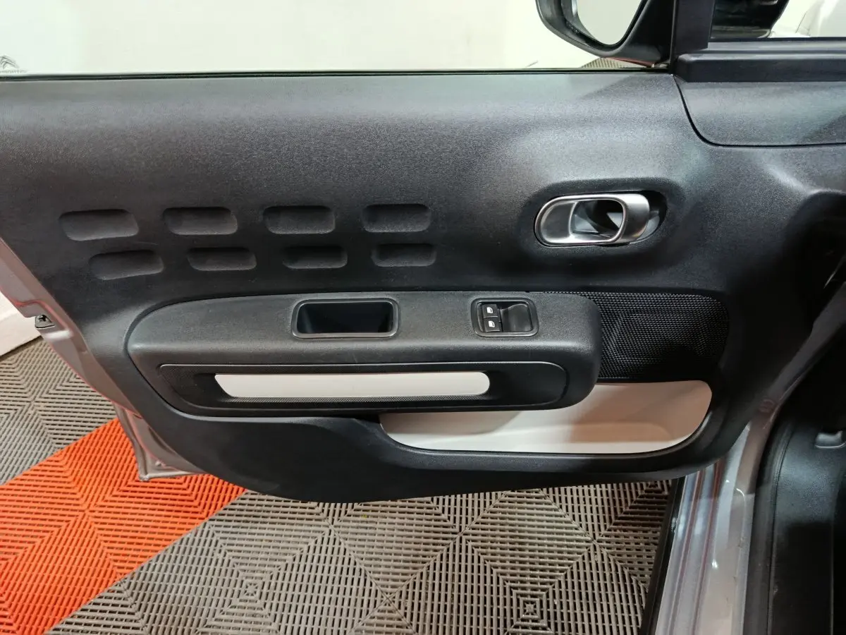 Vue rapprochée de la porte avant gauche gris clair de la Citroën C3 avec poignée intérieure et commandes de vitres.