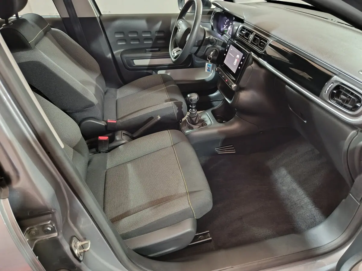 Vue intérieure côté conducteur de la Citroën C3 gris clair 2024, montrant sièges tissu, volant multifonctions et écran tactile central.