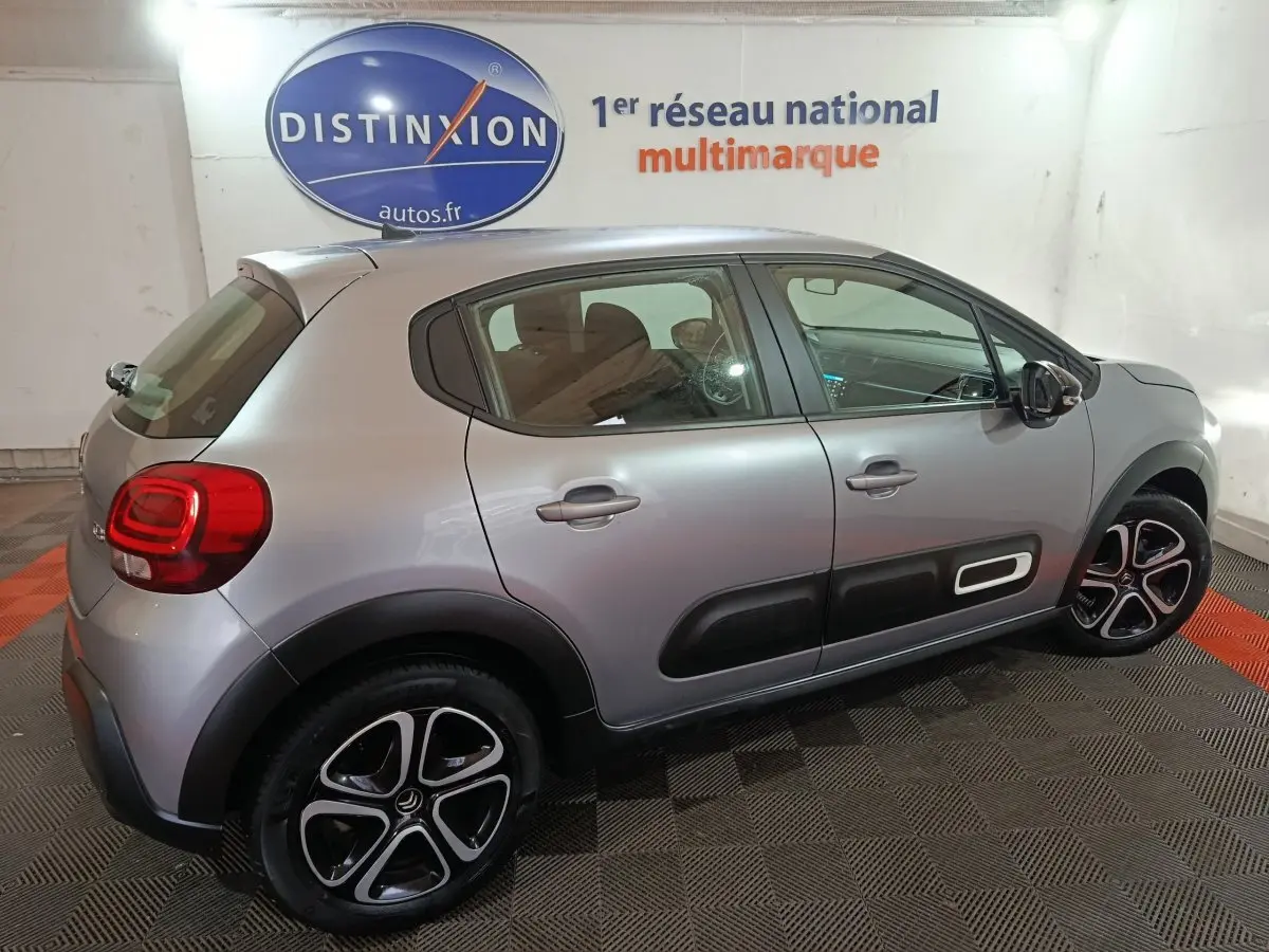 Vue côté droit en 3/4 arrière d'une Citroën C3 gris clair avec protections latérales noires et jantes alliage bicolores.