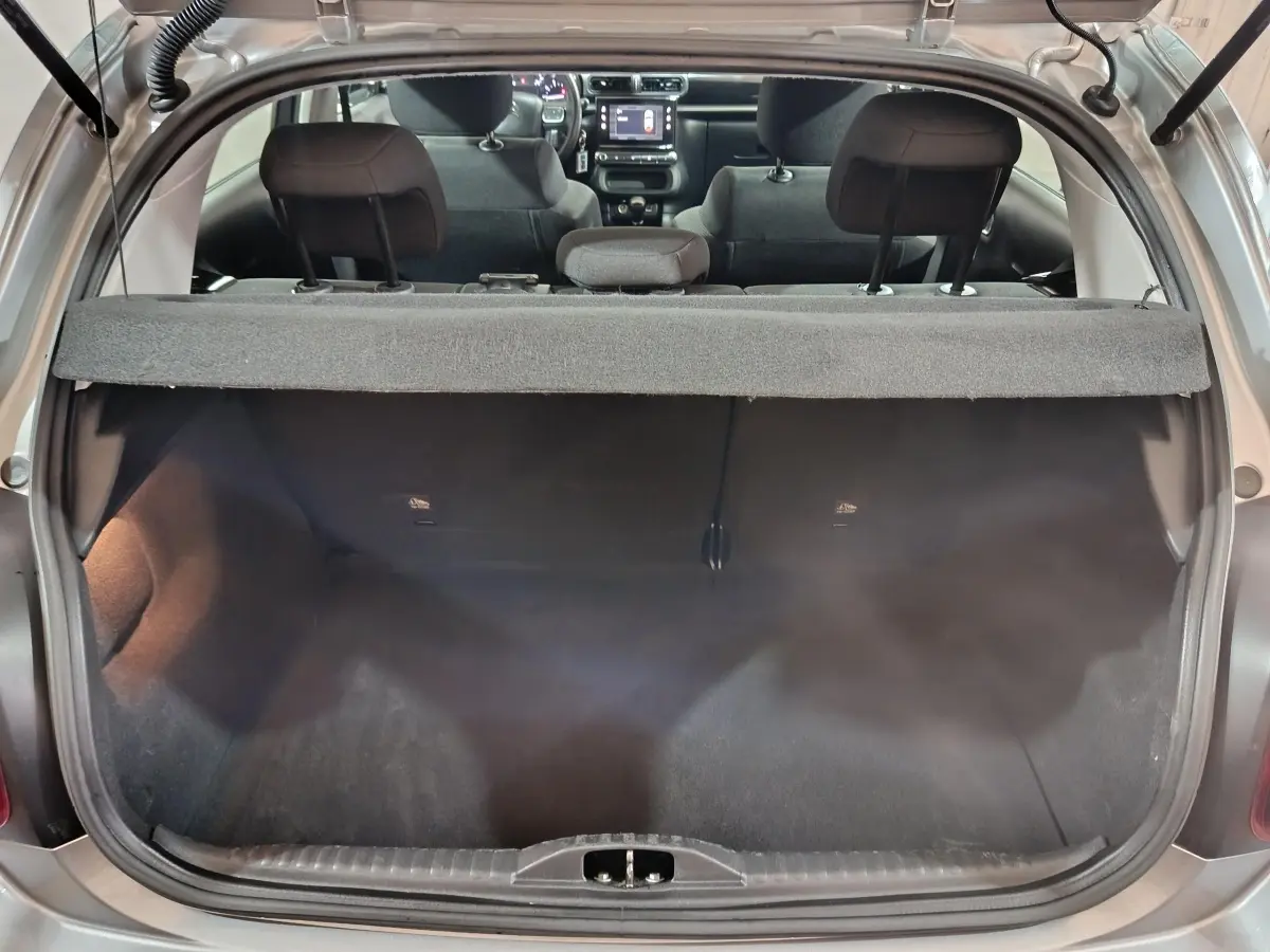 Vue arrière du coffre ouvert d'une Citroën C3 gris clair 2024, avec banquette arrière et tableau de bord visibles.