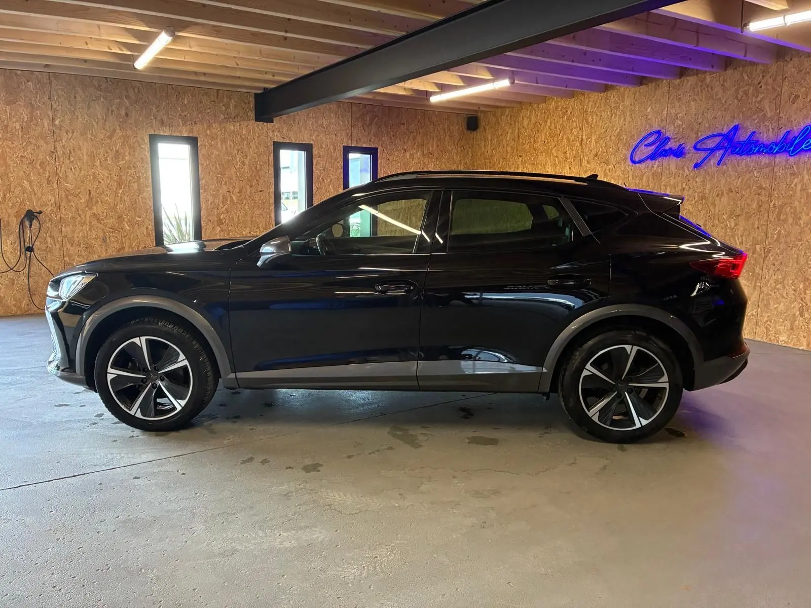 Vue de profil côté gauche d'un CUPRA Formentor noir 2022 avec jantes alu et toit noir piano dans un garage.