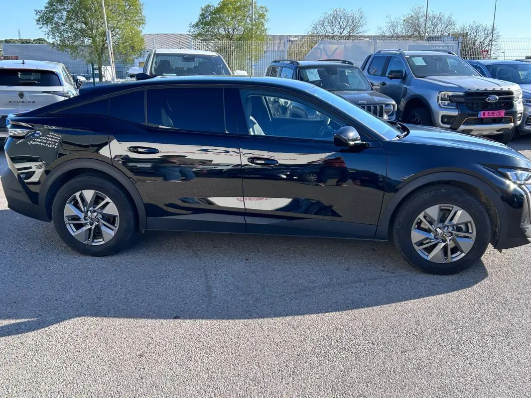 Vue latérale droite d'une Peugeot 408 PHEV 180 e-EAT8 Allure noire avec jantes alliage 17 pouces, stationnée en extérieur.