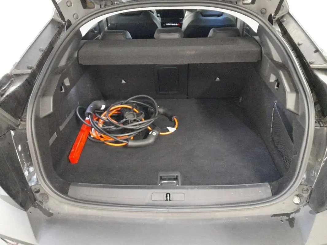 Coffre ouvert vu de l'arrière d'une Peugeot 408 PHEV noire, avec câble de recharge hybride et tapis noir.