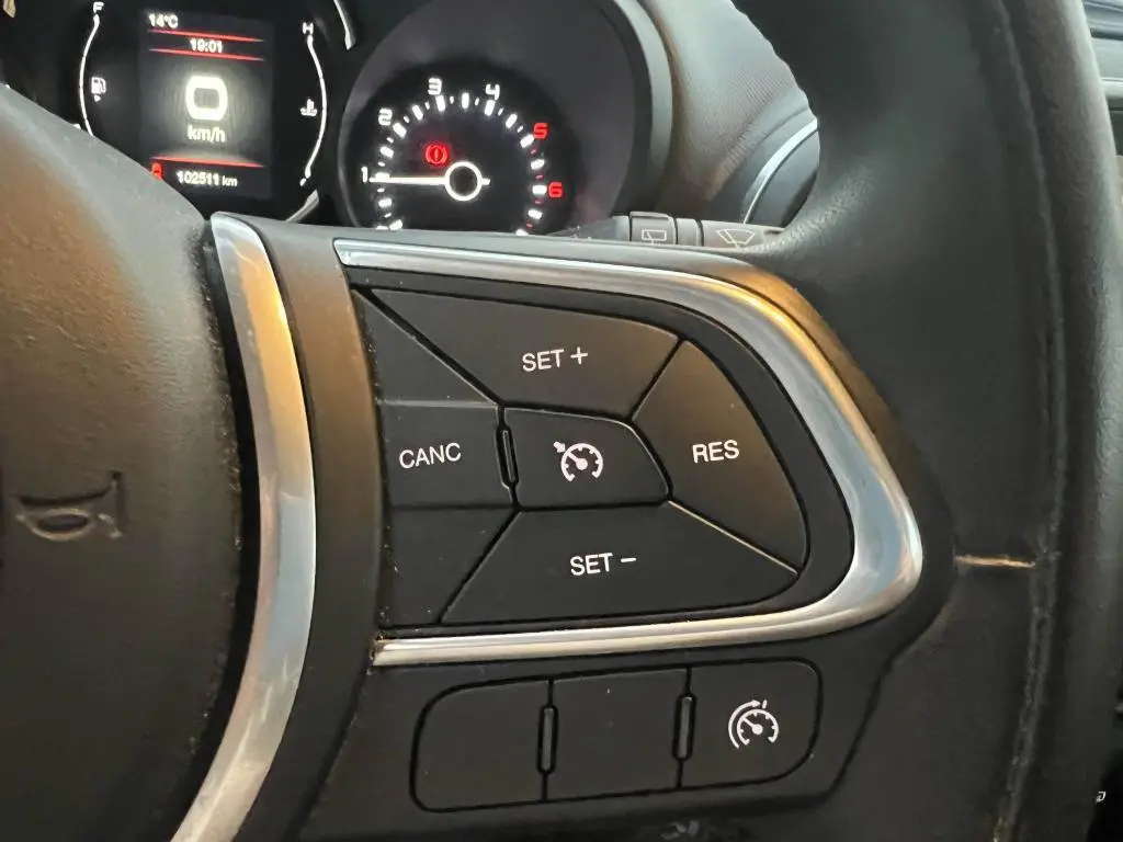 Gros plan sur les commandes du régulateur de vitesse au volant d'une Fiat 500L 2017, tableau de bord en arrière-plan.