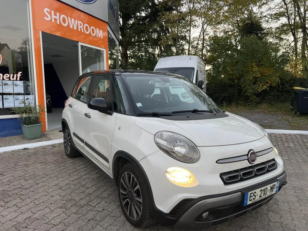 Vue 3/4 avant droite d'une Fiat 500L Lounge bi-color blanc et toit noir avec feux allumés devant un showroom