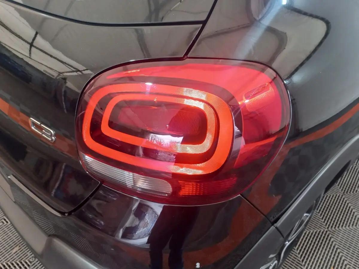 Gros plan sur le feu arrière droit rouge et noir brillant de la Citroën C3 BlueHDi 100 BVM PLUS 2024.