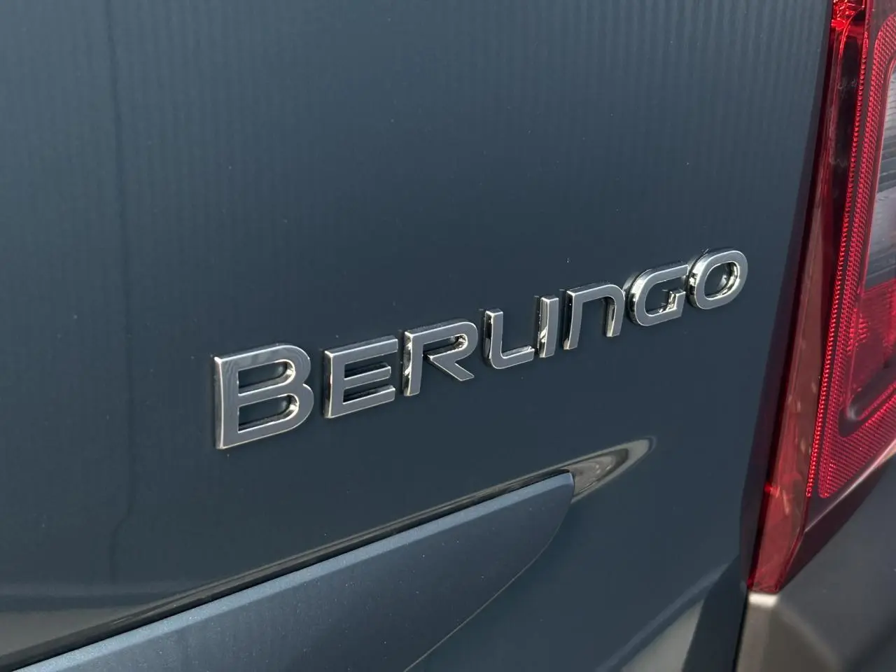 Gros plan sur l'arrière droit bleu métallisé du Citroën Berlingo avec logo et feu arrière rouge visible.
