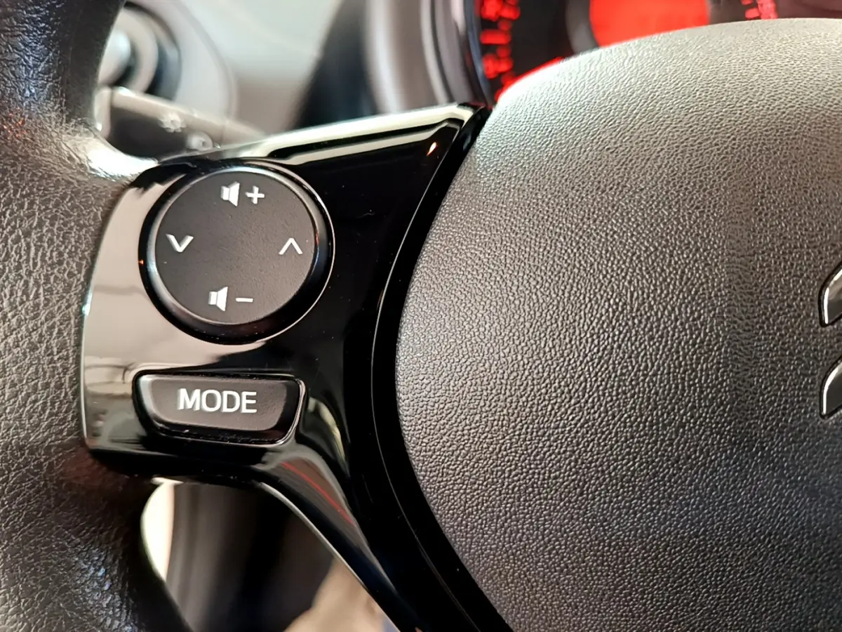 Gros plan sur les commandes noires du volant de la Citroën C1 blanche, mettant en avant les boutons de volume et mode.
