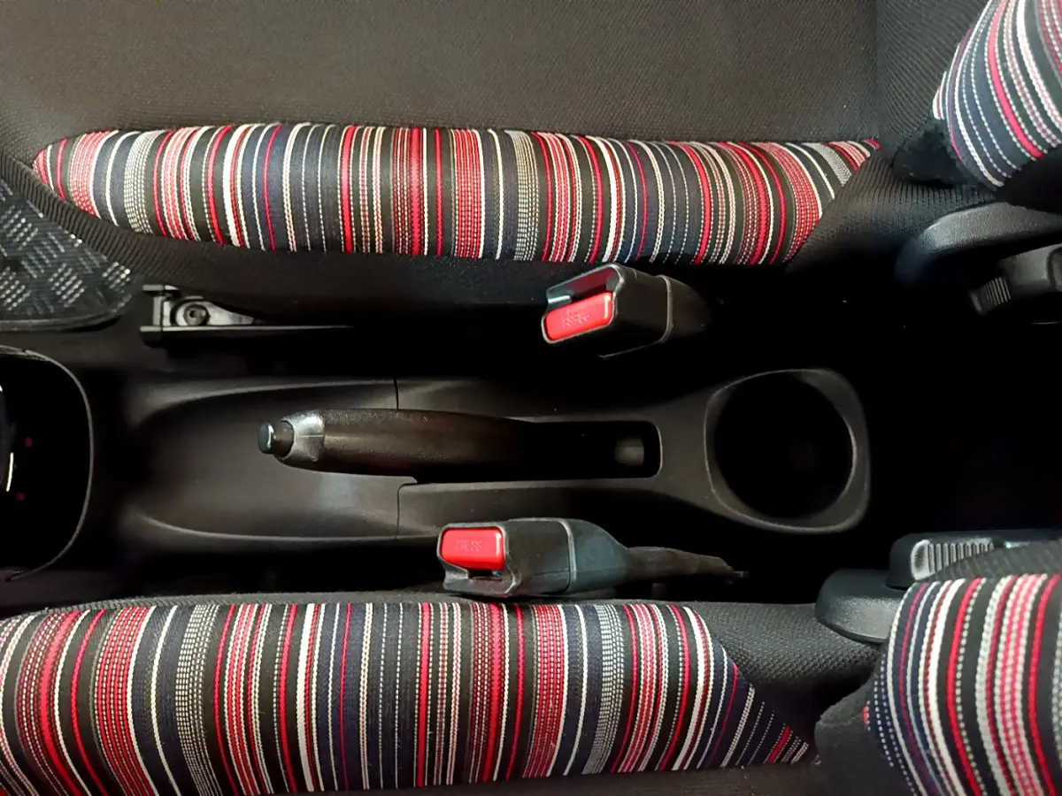 Vue plongeante sur la console centrale de la Citroën C1 blanche, avec frein à main et sièges rayés rouges, noirs et blancs.