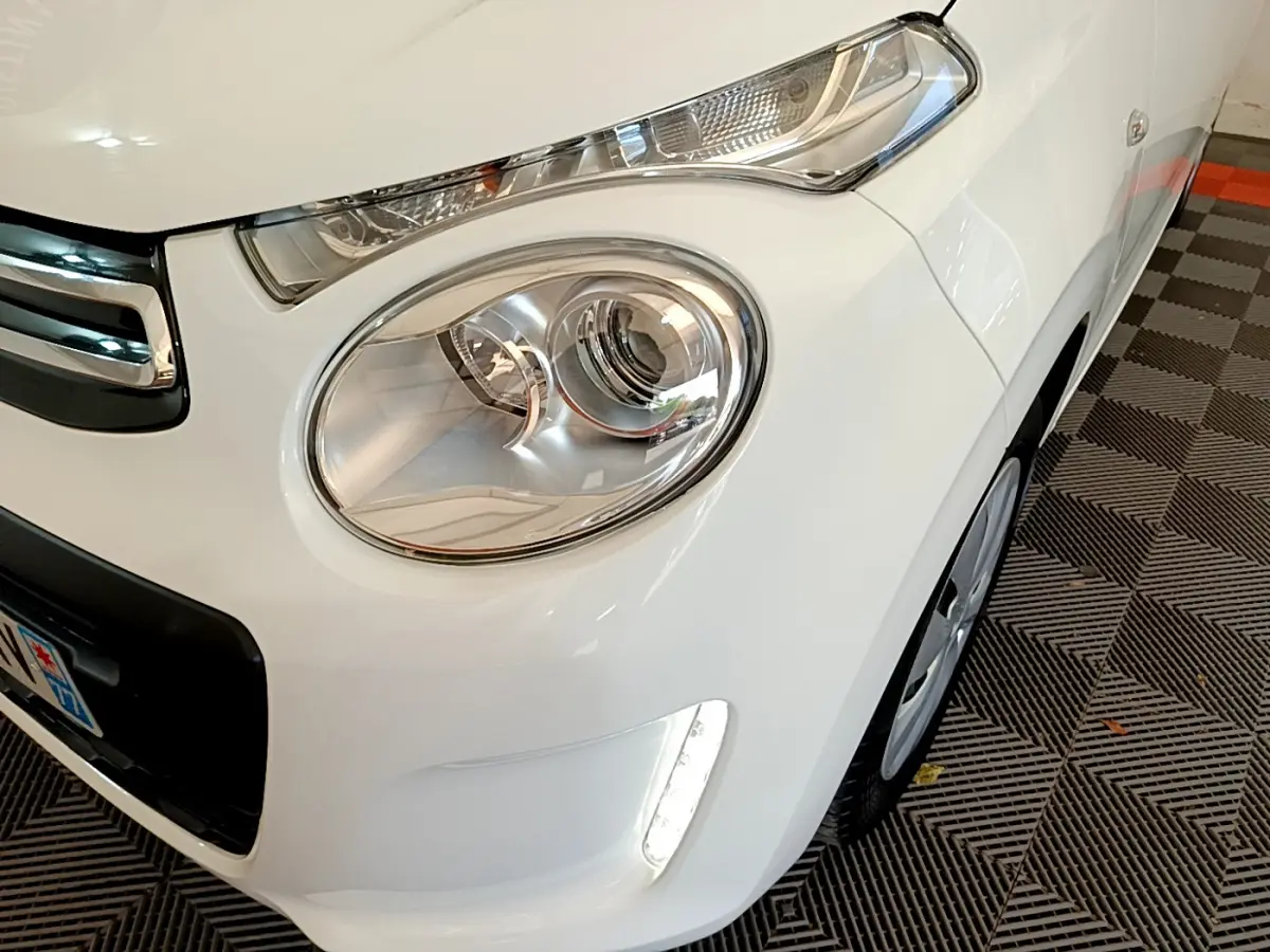Gros plan sur l'avant droit blanc d'une Citroën C1 2020, mettant en valeur le phare rond et la LED verticale.