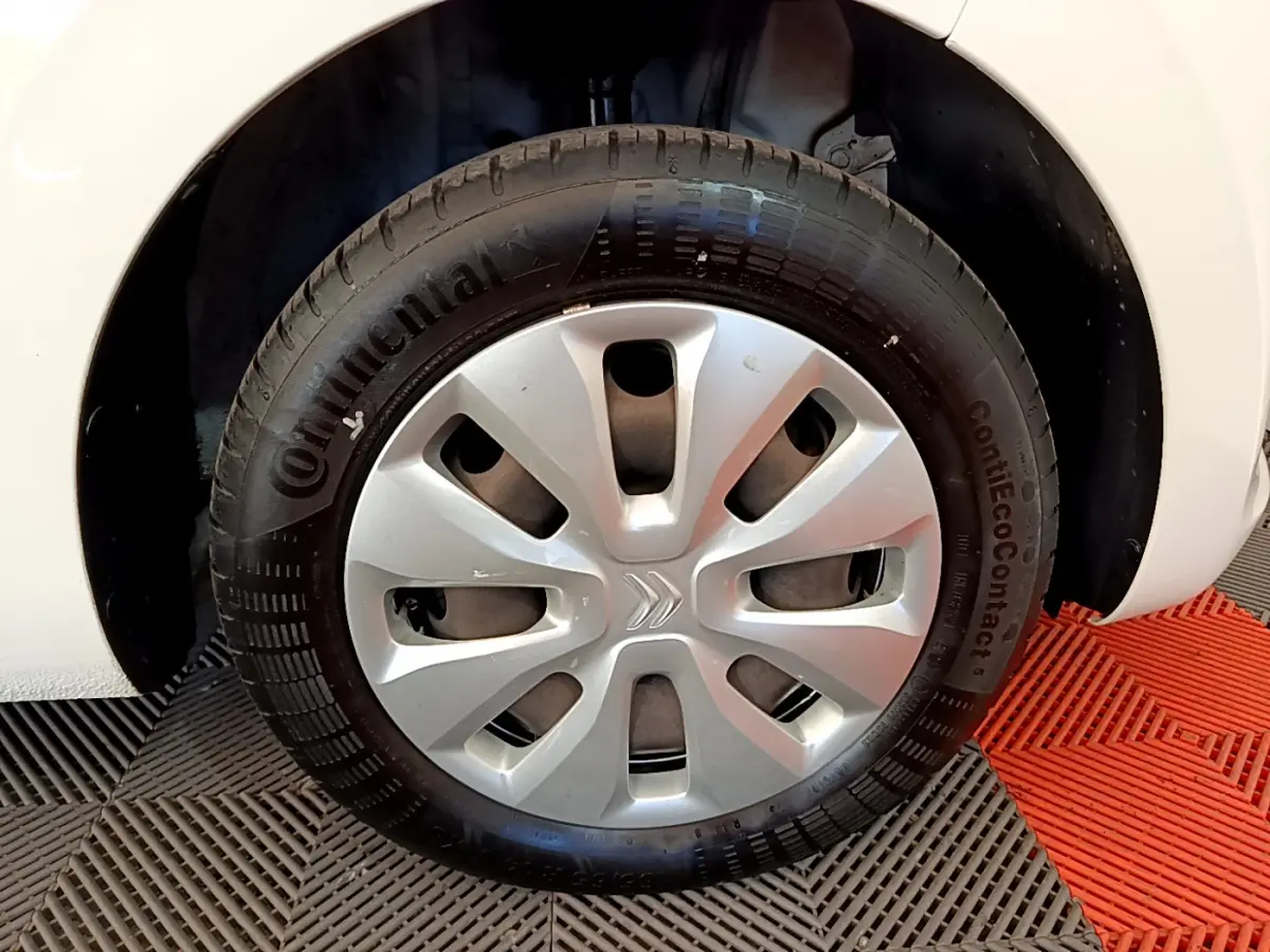 Gros plan sur la roue avant droite blanche d'une Citroën C1 VTi 72 S&S BVM Feel avec enjoliveur argenté.