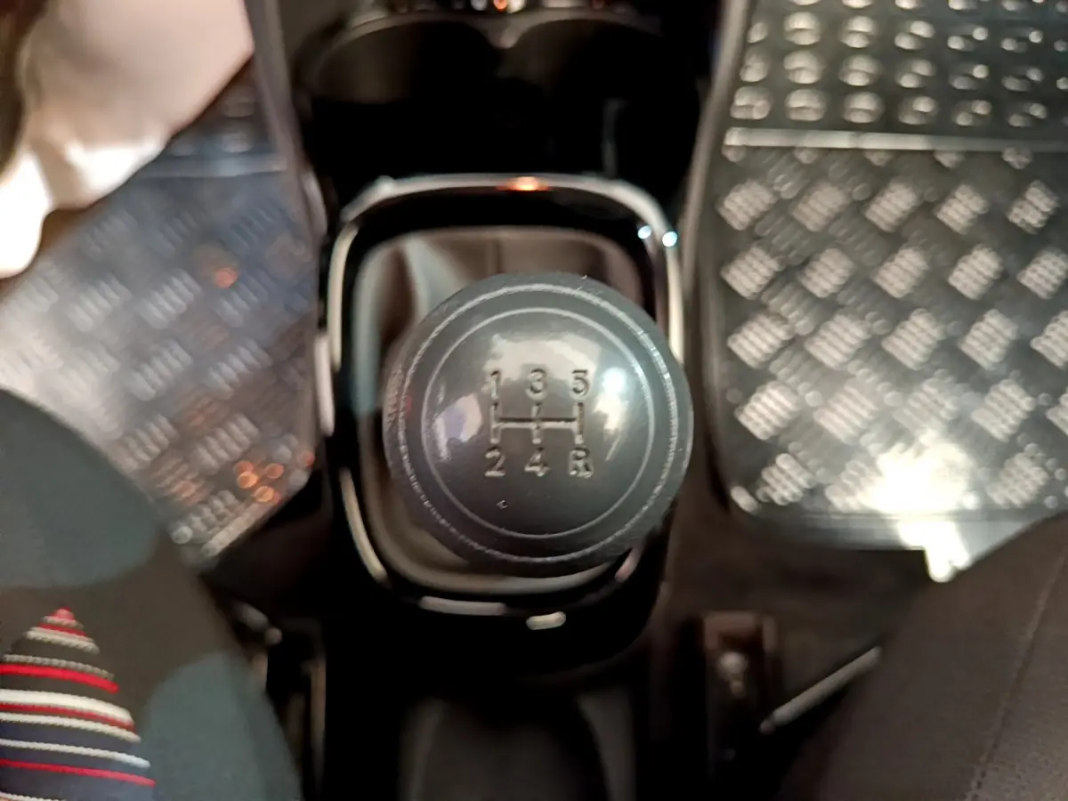 Gros plan sur le levier de vitesses manuel noir de la Citroën C1 blanche, entouré des sièges avant et tapis métallisés.