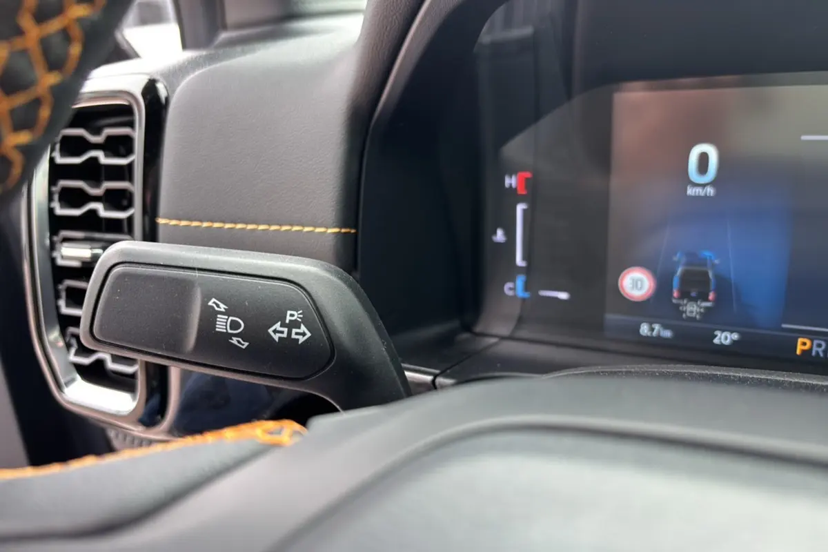 Détail du commodo gauche et tableau de bord numérique du Ford Ranger Wildtrak Plus noir agate, avec surpiqûres orange.