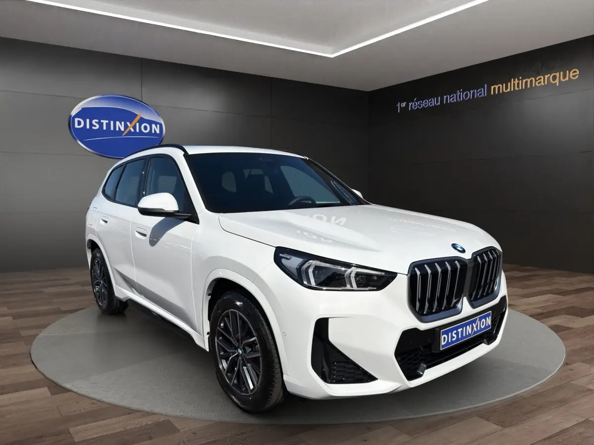 BMW X1 sDrive20d blanc vue de profil côté gauche avec jantes noires en showroom intérieur