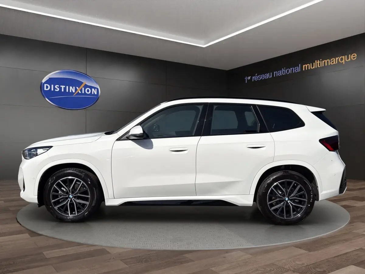 Vue arrière d'un BMW X1 blanc sDrive20d M SPORT avec diffuseur noir et feux LED distinctifs.