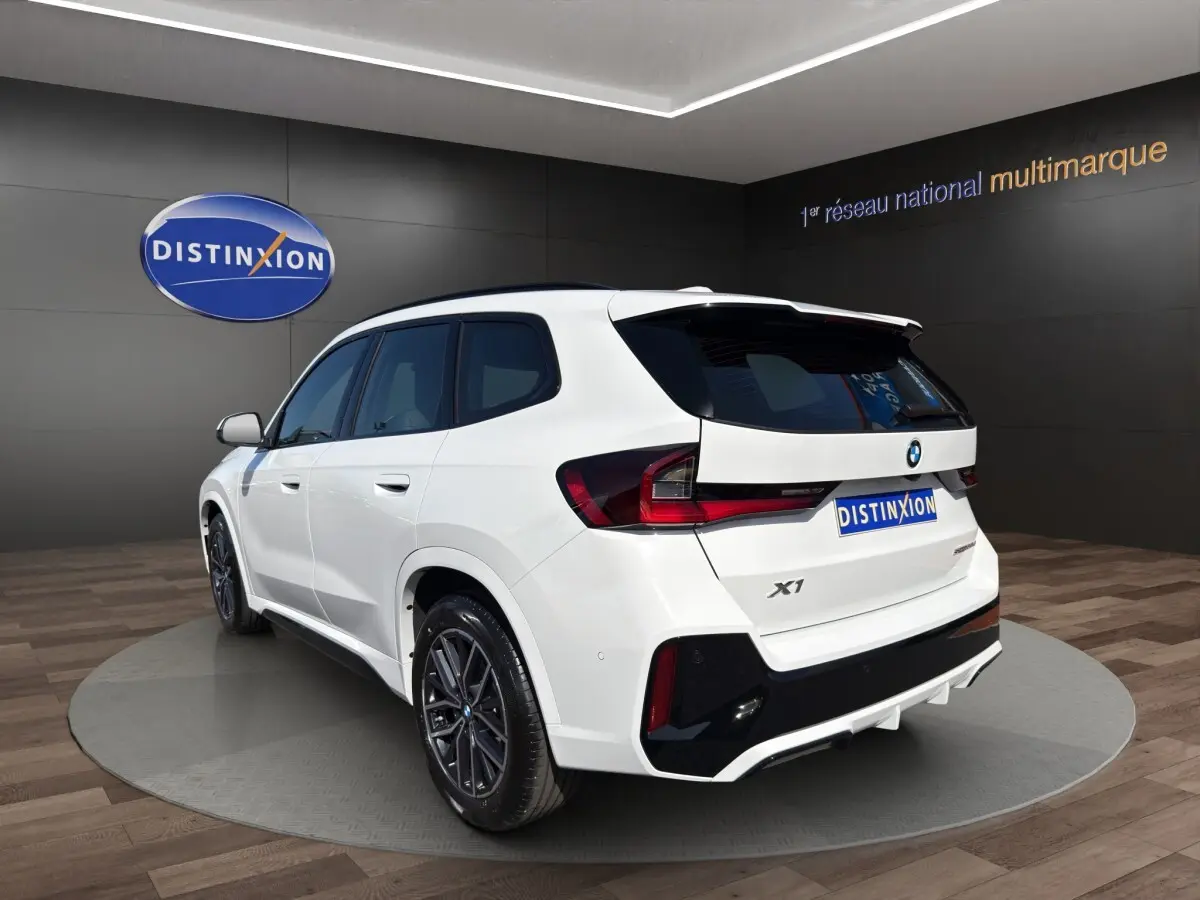 BMW X1 sDrive20d blanc en 3/4 arrière droit avec toit noir et jantes sport dans showroom