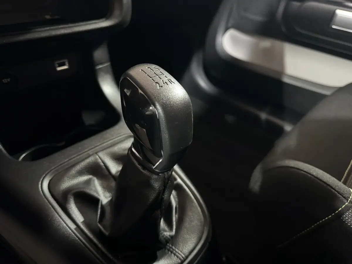 Gros plan sur le levier de vitesses manuel noir de la Citroën C3 PureTech 82, intérieur sombre avec coutures visibles.