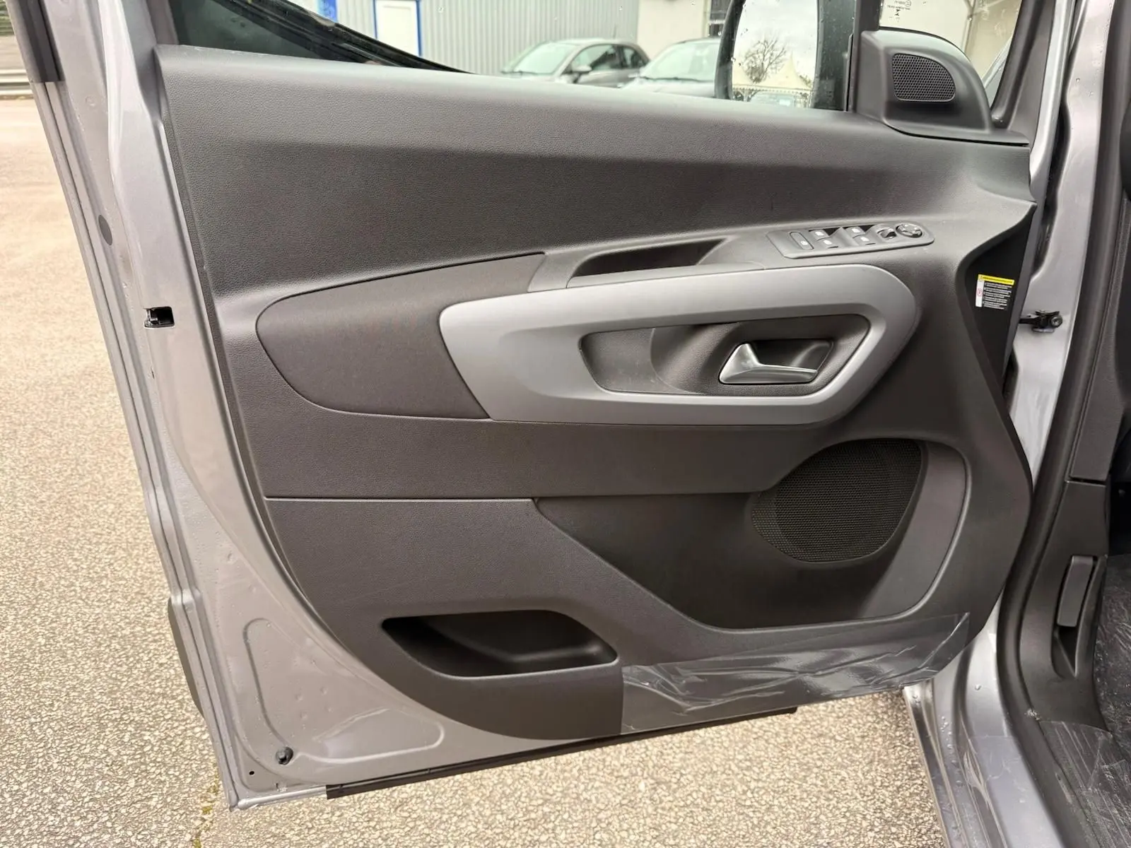 Vue intérieure de la porte avant gauche du Citroën Berlingo gris Artense, avec commandes électriques et poignée intégrée.