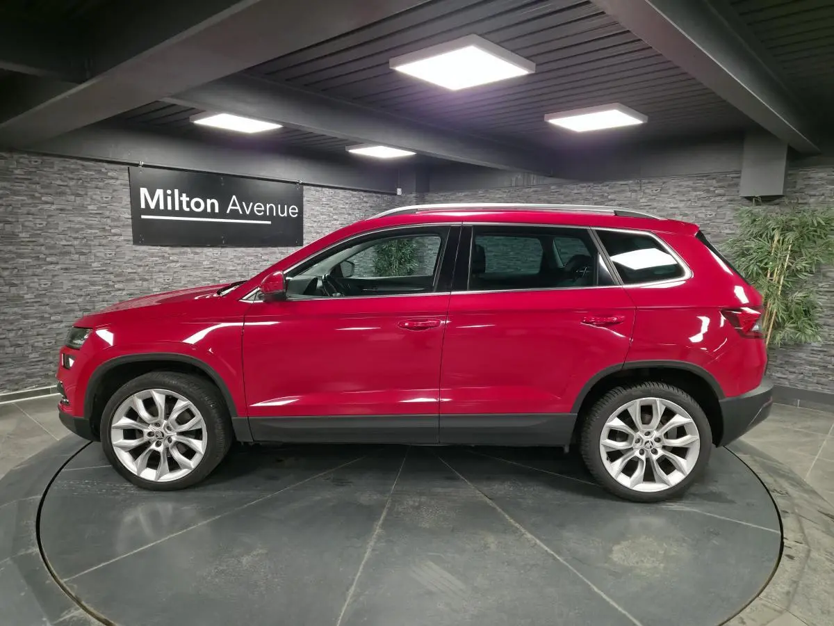 Profil droit d'un Skoda Karoq rouge avec jantes alliage 19 pouces dans un showroom intérieur.