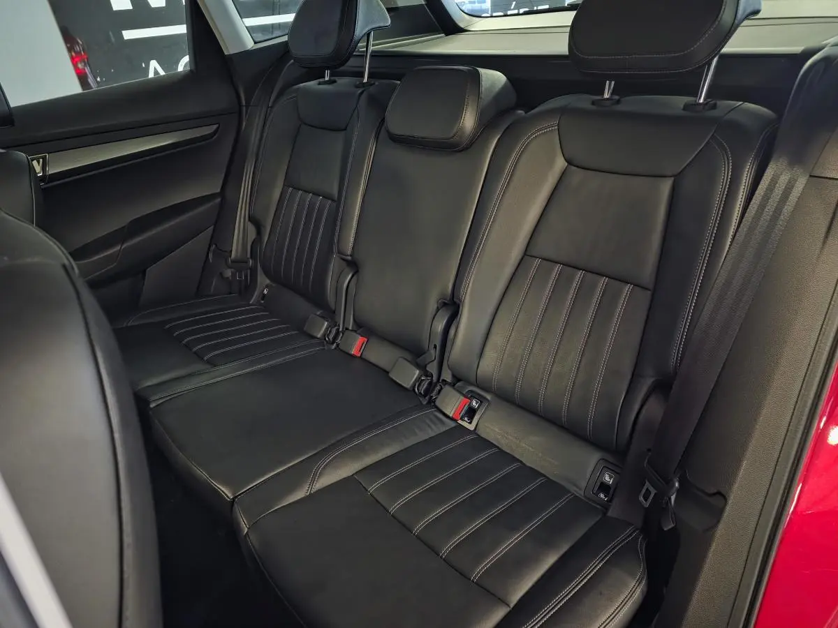 Vue intérieure des sièges arrière en cuir noir du Skoda Karoq rouge, avec ceintures de sécurité et appuie-têtes visibles.