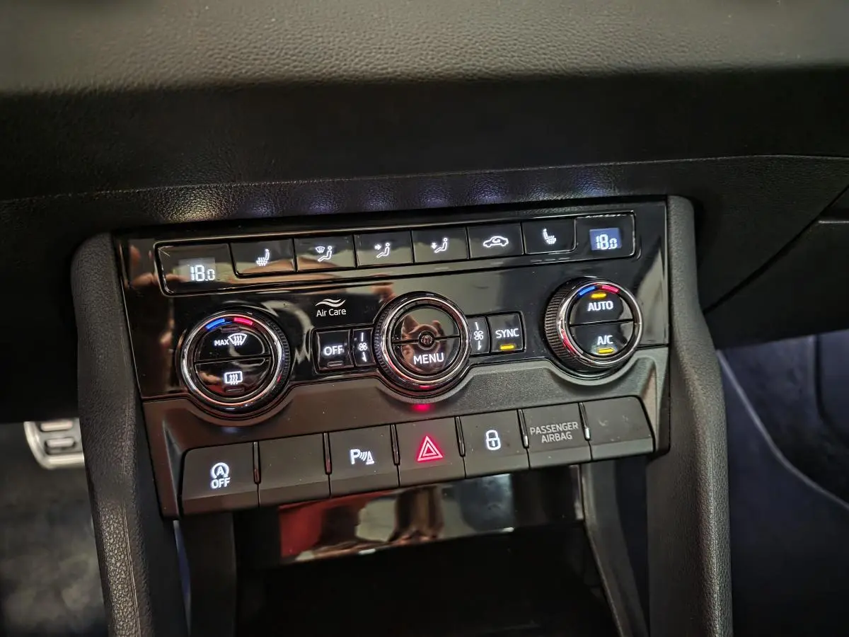 Panneau de commande de climatisation noir brillant dans l'habitacle d'une Skoda Karoq rouge, avec réglages digitaux à 18°C.