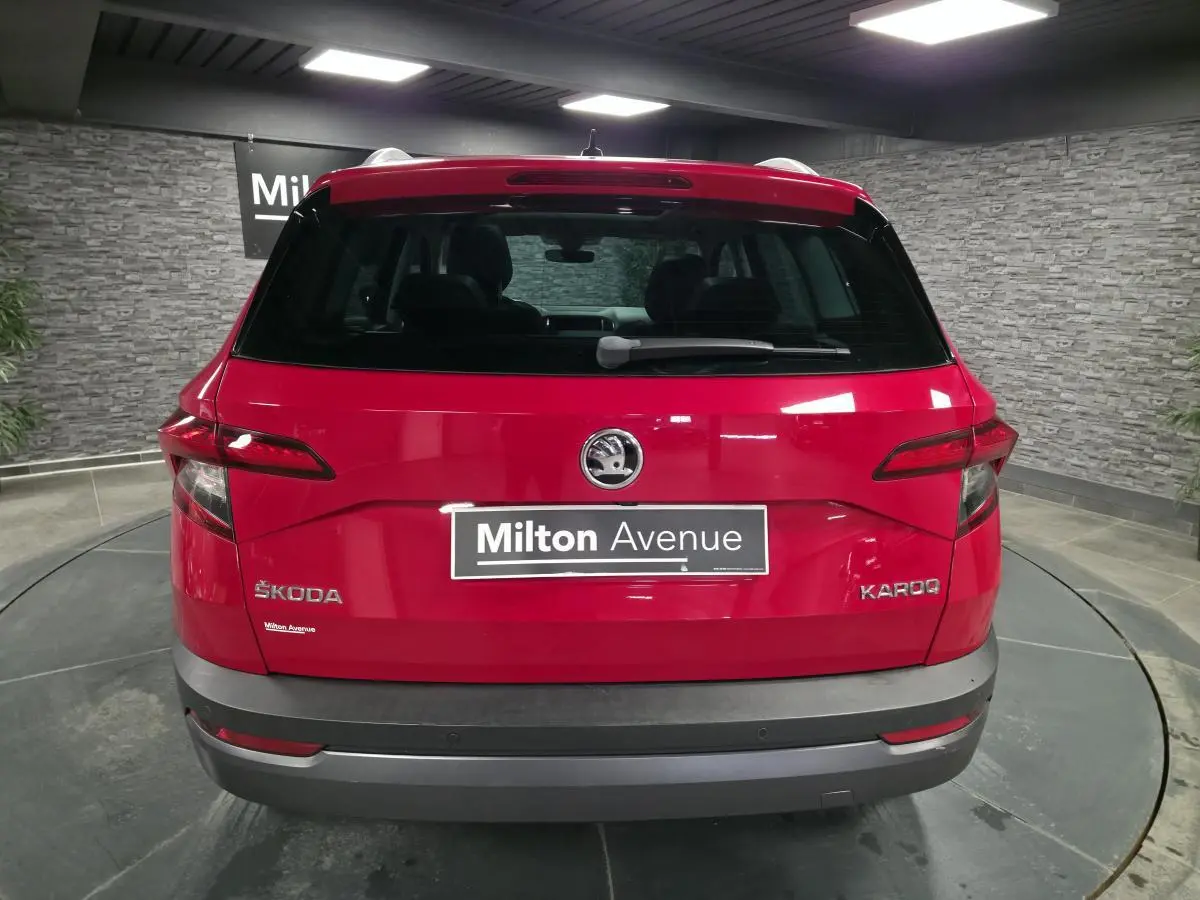 Vue arrière d'un Skoda Karoq rouge avec logo et plaque Milton Avenue dans un showroom intérieur.