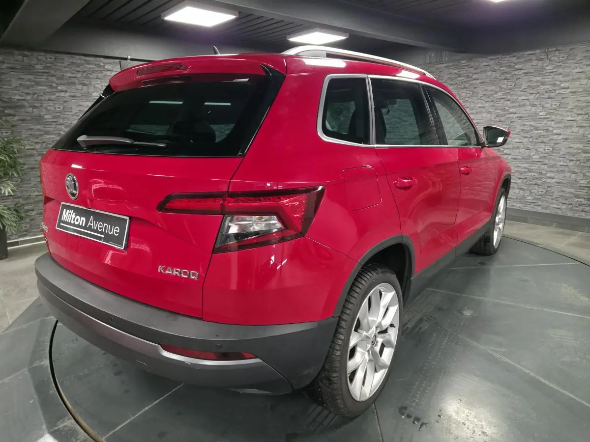 Vue 3/4 arrière droite d'un Skoda Karoq rouge avec jantes alliage argent et hayon fermé en intérieur showroom.