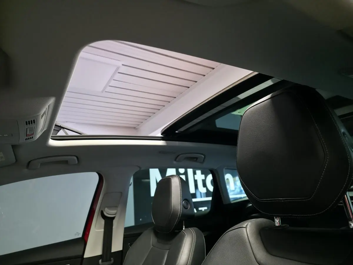 Toit ouvrant panoramique ouvert vu de l'intérieur avant d'un Skoda Karoq rouge avec sièges cuir noirs.