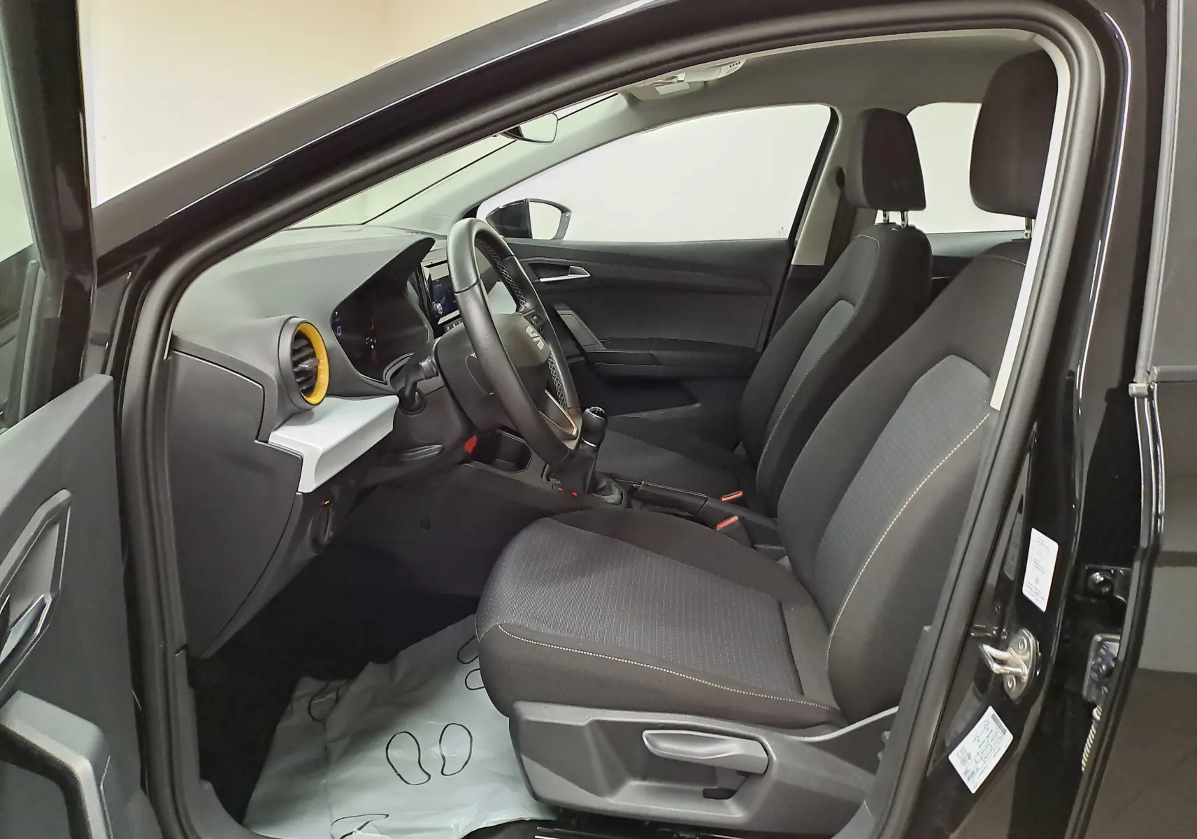 Intérieur côté conducteur du SEAT Ibiza 2024 noir minuit, vue de profil montrant sièges et tableau de bord avec airbag jaune.