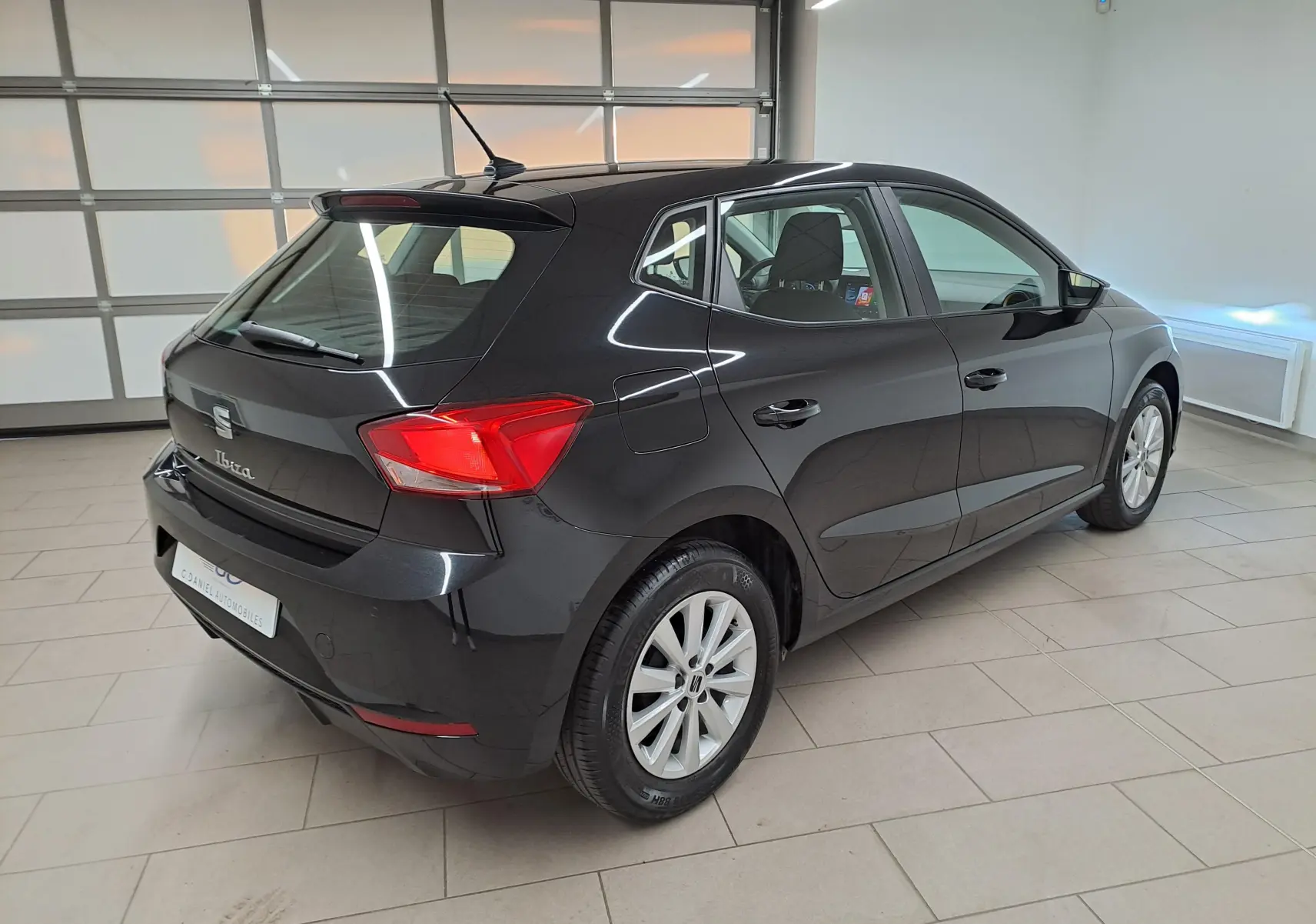 Vue 3/4 arrière droite d'une SEAT Ibiza 2024 noir minuit, avec feux arrière rouges et jantes argentées en intérieur showroom.