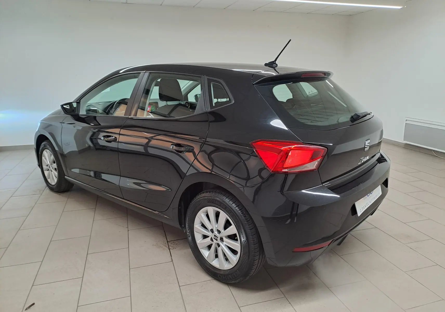 Vue 3/4 arrière droite d'une SEAT Ibiza 2024 noire minuit, avec feux arrière rouges et jantes alliage argentées.