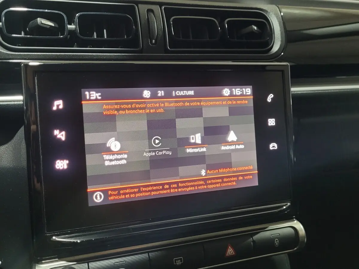 Écran tactile central allumé dans l’habitacle noir d’une Citroën C3 beige, vue de face rapprochée.