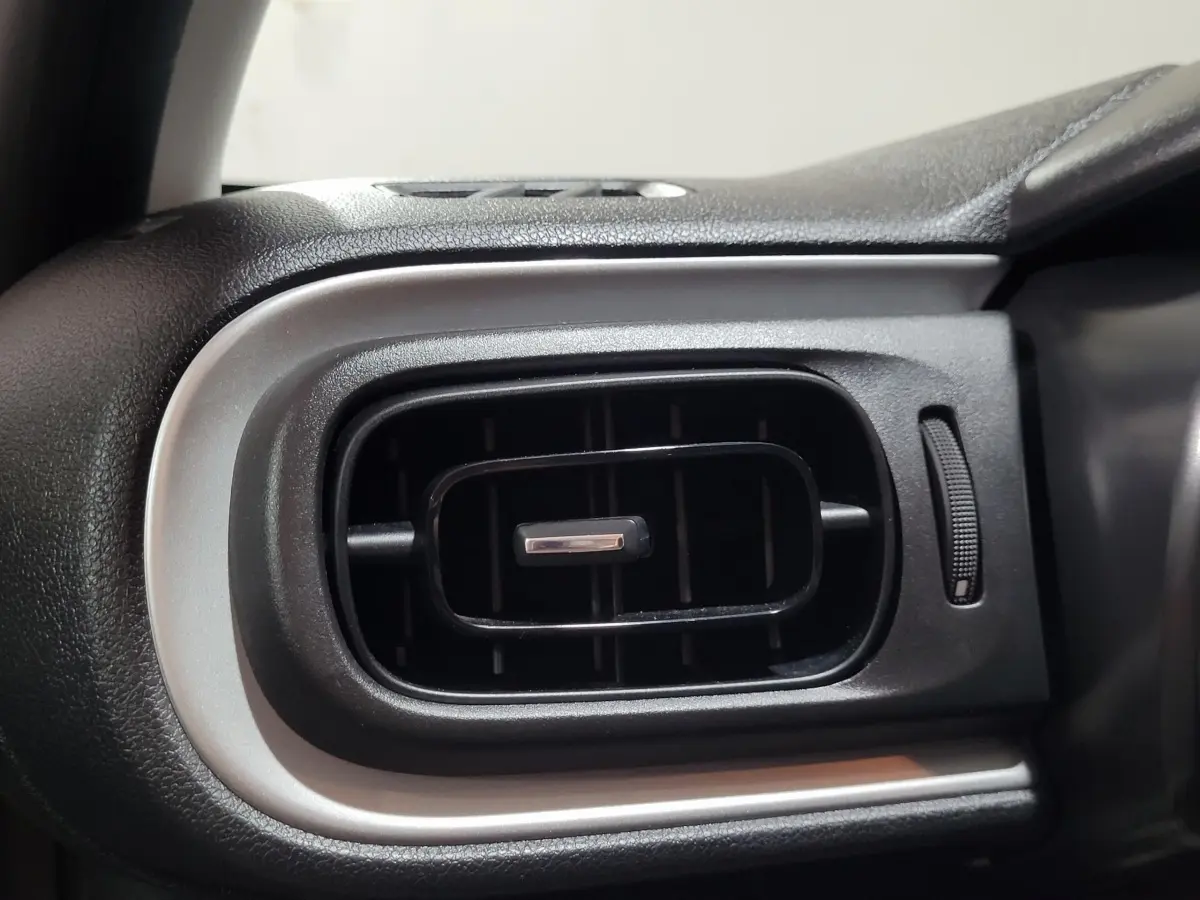 Gros plan sur la sortie d’air rectangulaire noire avec contour argenté du tableau de bord intérieur d’une Citroën C3 beige.
