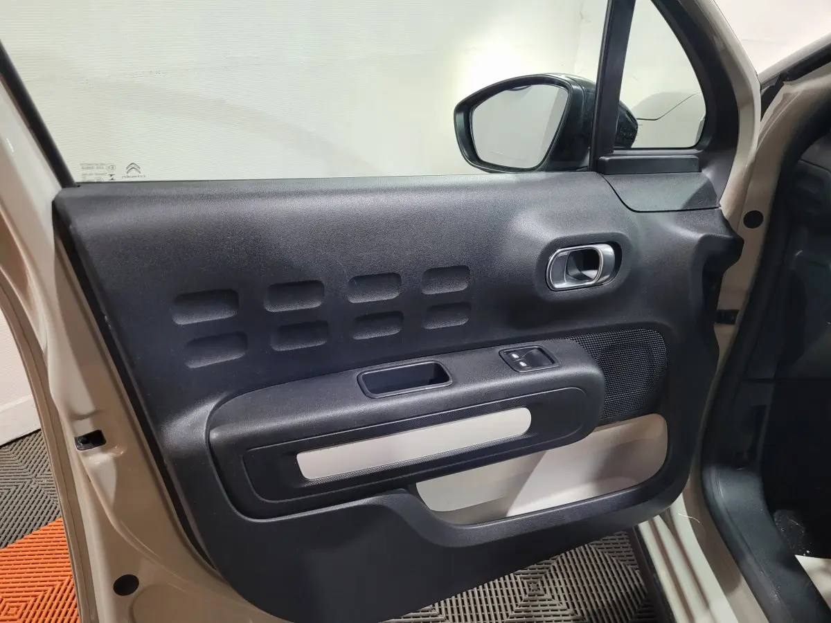 Vue intérieure de la porte avant gauche beige de la Citroën C3 2022 avec poignée argentée et commande de vitre.